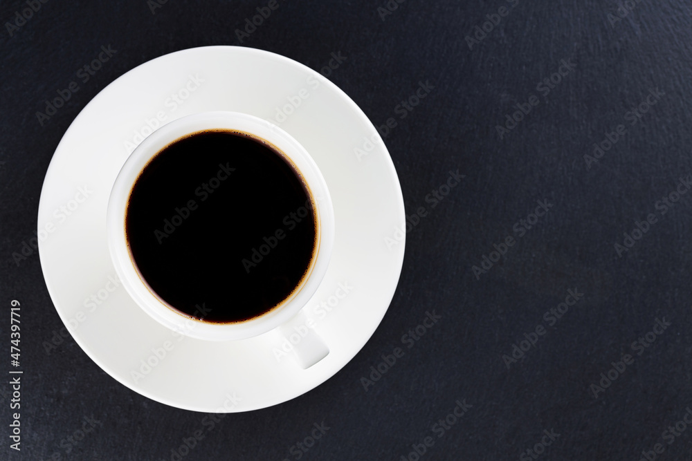Cup of black coffee on a white saucer. Morning coffee in ceramic cup on a dark background. Top view. Copy space Cup of black coffee on a white saucer. Morning coffee in ceramic cup on a dark background. Top view. Copy space