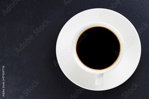 Cup of black coffee on a white saucer. Morning coffee in ceramic cup on a dark background. Top view. Copy space © Lazarenko O.