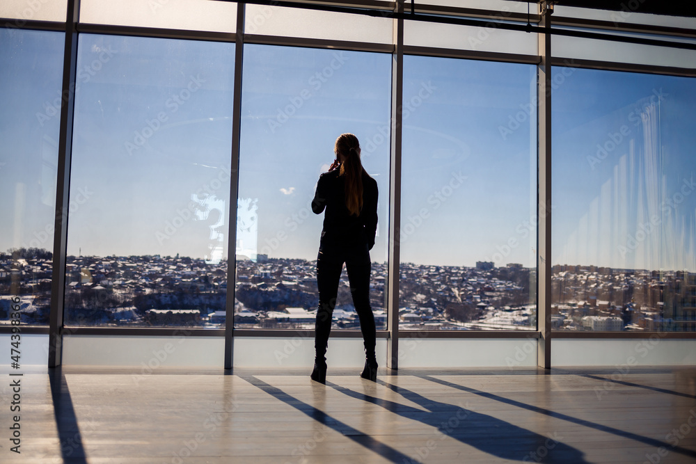 Rear view of a businessman looking out of a large window overlooking the city. He has a phone in his hands. Horizontal view. Rear view of a businessman looking out of a large window overlooking the city. He has a phone in his hands. Horizontal view.