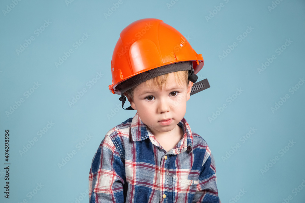 Serious little kid boy engineer or architect in a protective orange helmet Serious little kid boy engineer or architect in a protective orange helmet