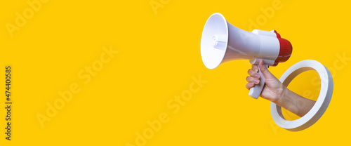 Female hand holds a megaphone in a round hole on a yellow background. Banner.