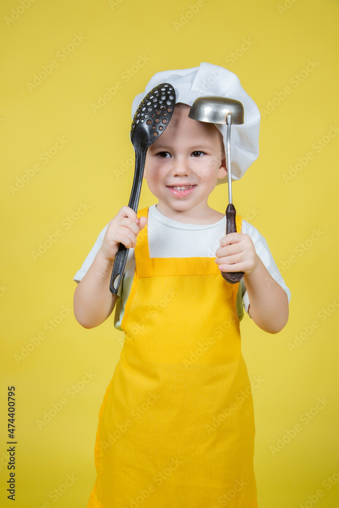 Boy in apron and chef's hat holds a ladle and slotted spoon Boy in apron and chef's hat holds a ladle and slotted spoon