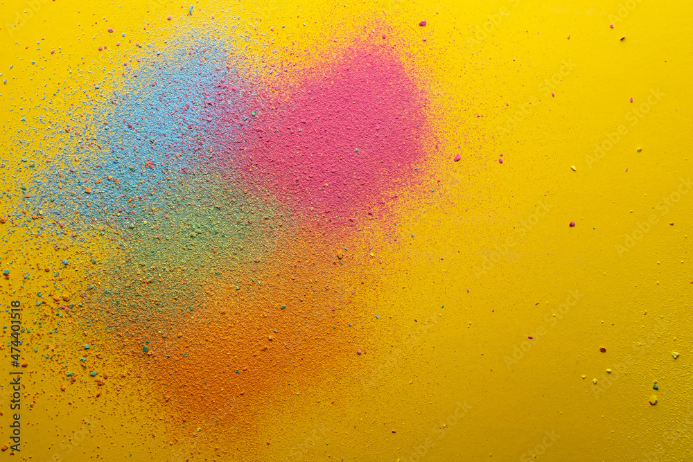 Multicolored, bright powder scattered on a yellow background. Copy space. Abstract texture. Top view. 