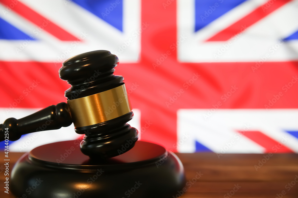 Closeup of isolated judge wood gavel with blurred english flag background (focus on hammer head)
