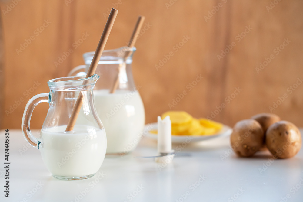 Vegan plant milk from potato in glass jar and potato tubers on the table. Concept of potato milk, vegan sustainable option, plant-based dairy. Substitute drink, healthy eating, diet, nutrition