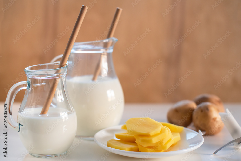 Vegan plant milk from potato in glass jar and potato tubers on the table. Concept of potato milk, vegan sustainable option, plant-based dairy. Substitute drink, healthy eating, diet, nutrition Vegan plant milk from potato in glass jar and potato tubers on the table. Concept of potato milk, vegan sustainable option, plant-based dairy. Substitute drink, healthy eating, diet, nutrition