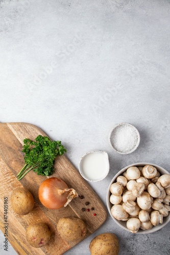 Ingredients for mushroom cream soup on grey table. Champignon, cream, potatoes, onions, parsley, salt and spices on wooden board. Top view, copy space.