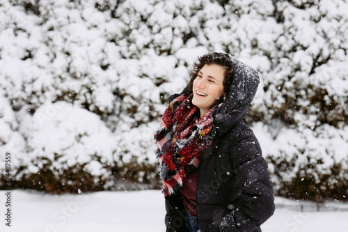 Woman in hood and red scarf smiling and laughing outside on snow