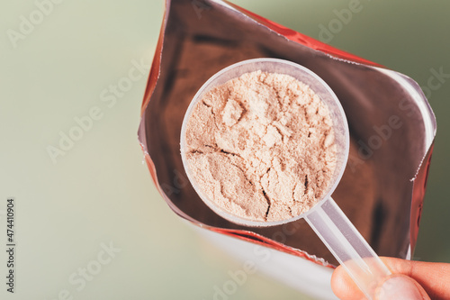 Close-up whey protein measuring spoon over open package bag photo