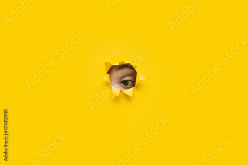 Eye looking through a hole in a yellow paper. Voyeurism. Woman is watching the husband. A curious look. Jealousy, spying on or overhearing the concept. Copy space. photo