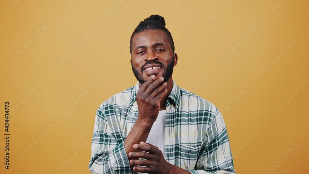 Young African American male smiling, acting like looking into mirror, straightening beard. Posing on beige background. Close up, copy space Young African American male smiling, acting like looking into mirror, straightening beard. Posing on beige background. Close up, copy space