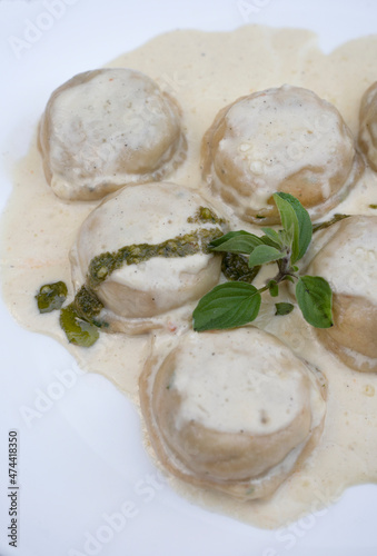 Italian food. Pasta. Closeup view of mozzarella cheese and ham sorrentinos with cream and pesto sauce, in a white dish. 