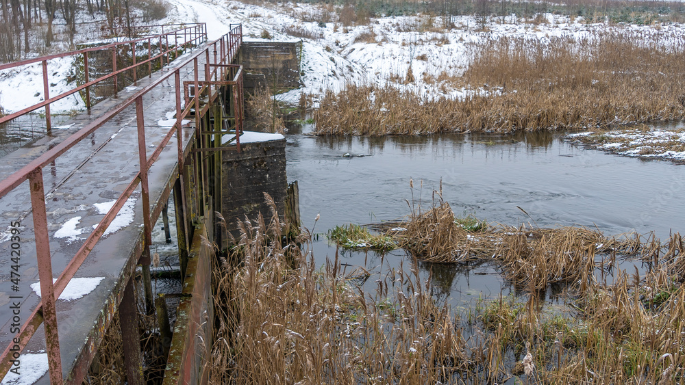 The narrow old wooden bridge over winter river. Wooden pedestrian bridge over river in countryside. Winter landscape. The narrow old wooden bridge over winter river. Wooden pedestrian bridge over river in countryside. Winter landscape.