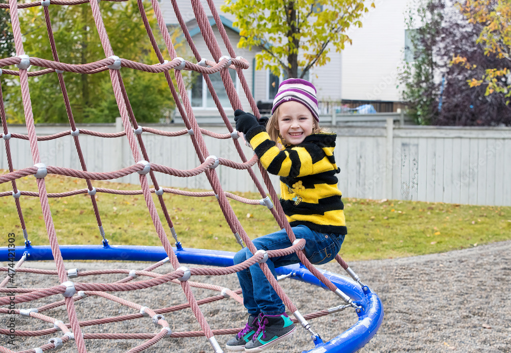 A young girl wearing a bumble bee sweater playing on a swing in a park.