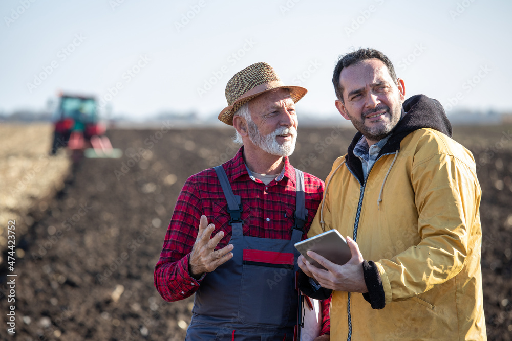 Fototapeta premium Farmers talking in field in front of tractor in autumn