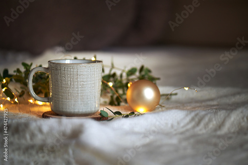 Ceramic glazed coffee mug on a beige knited background with eucaliptus leaves and christmas garland lights, concept Christmas cozy winter day at hugge home, selecive focus, copy space photo