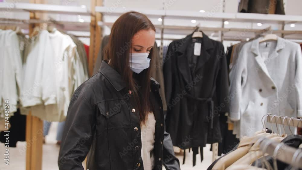 A woman in a medical mask measures a black jacket in a clothing store. A woman in a medical mask measures a black jacket in a clothing store.