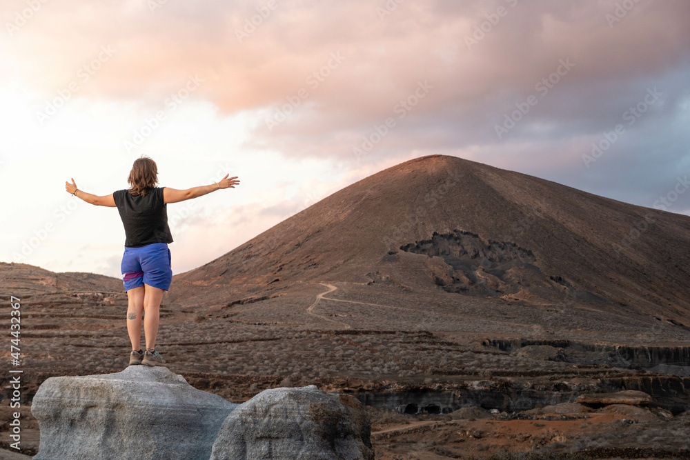 Mujer joven con los brazos abiertos admirando un paisaje volcánico al atardecer, Lanzarote, Islas Canarias, España. Mujer joven con los brazos abiertos admirando un paisaje volcánico al atardecer, Lanzarote, Islas Canarias, España.
