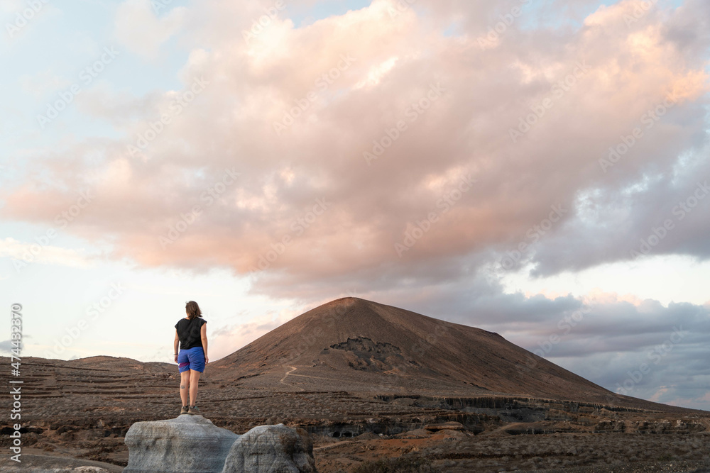 Mujer joven admirando un paisaje volcánico al atardecer, Lanzarote, Islas Canarias, España.