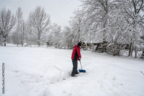 man in a red jacket cleans the road from snow with a shovel in the village. Winter worries