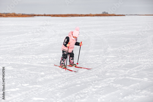 Little girl is skiing. Child in pink warm suit learns to ski snow on frosty winter day, winter landscape, snow background. 