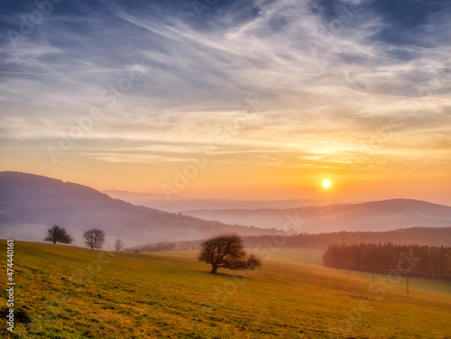 Scenic hilly landscape with solitary trees during sunset, view to the valley, blue sky with high clouds,sun. Autumn evening. White Carpathians mountains,Czech republic. .