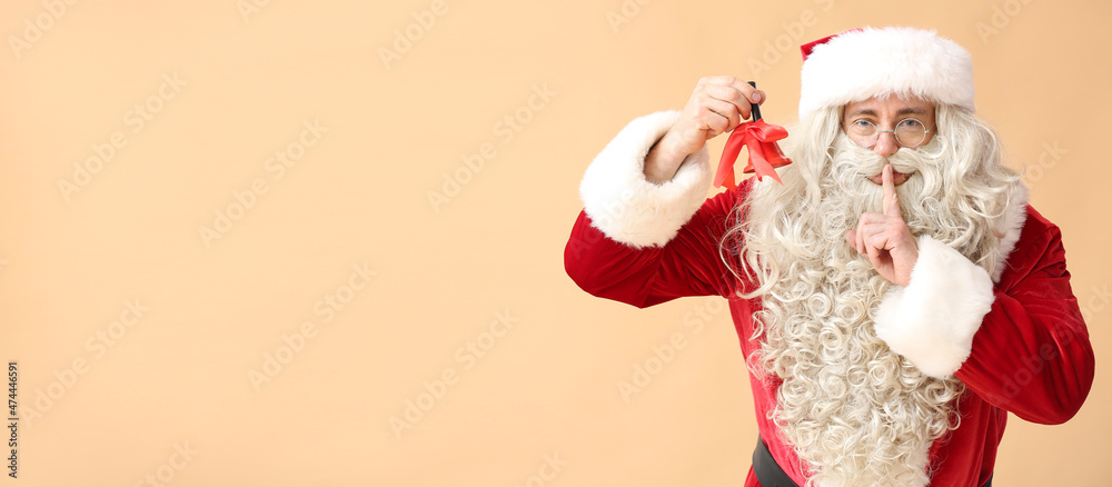 Santa Claus with Christmas bell showing silence gesture on beige background with space for text Santa Claus with Christmas bell showing silence gesture on beige background with space for text