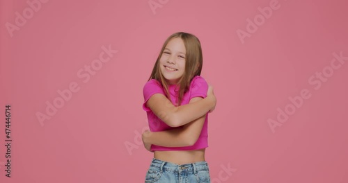 Pretty child girl embrace herself with love on pink studio background. Positive childish self-esteem, self-care