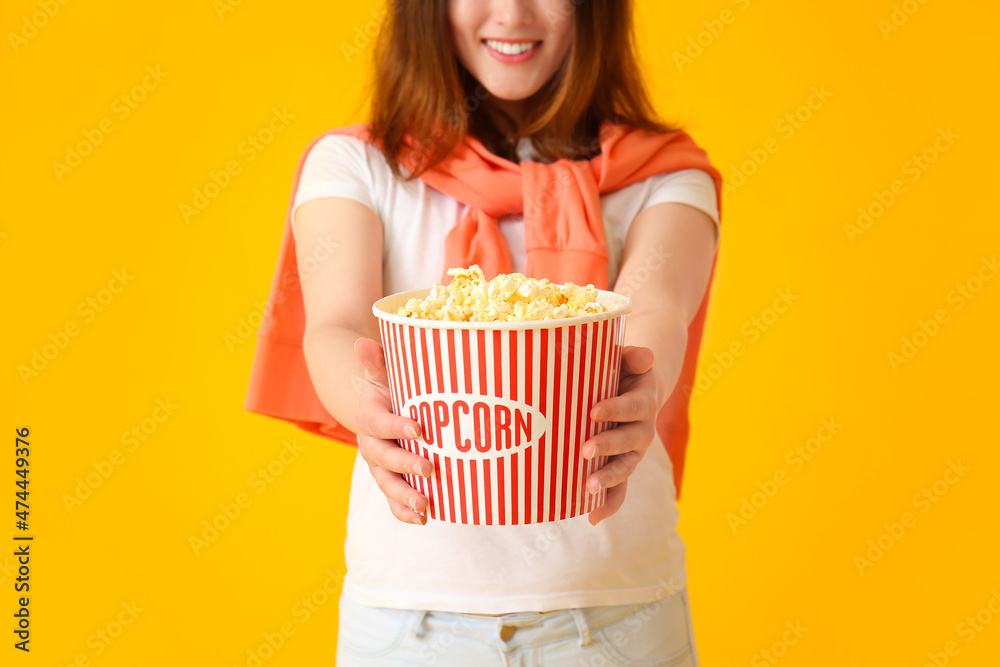 Young Asian woman with bucket of tasty popcorn on yellow background Young Asian woman with bucket of tasty popcorn on yellow background