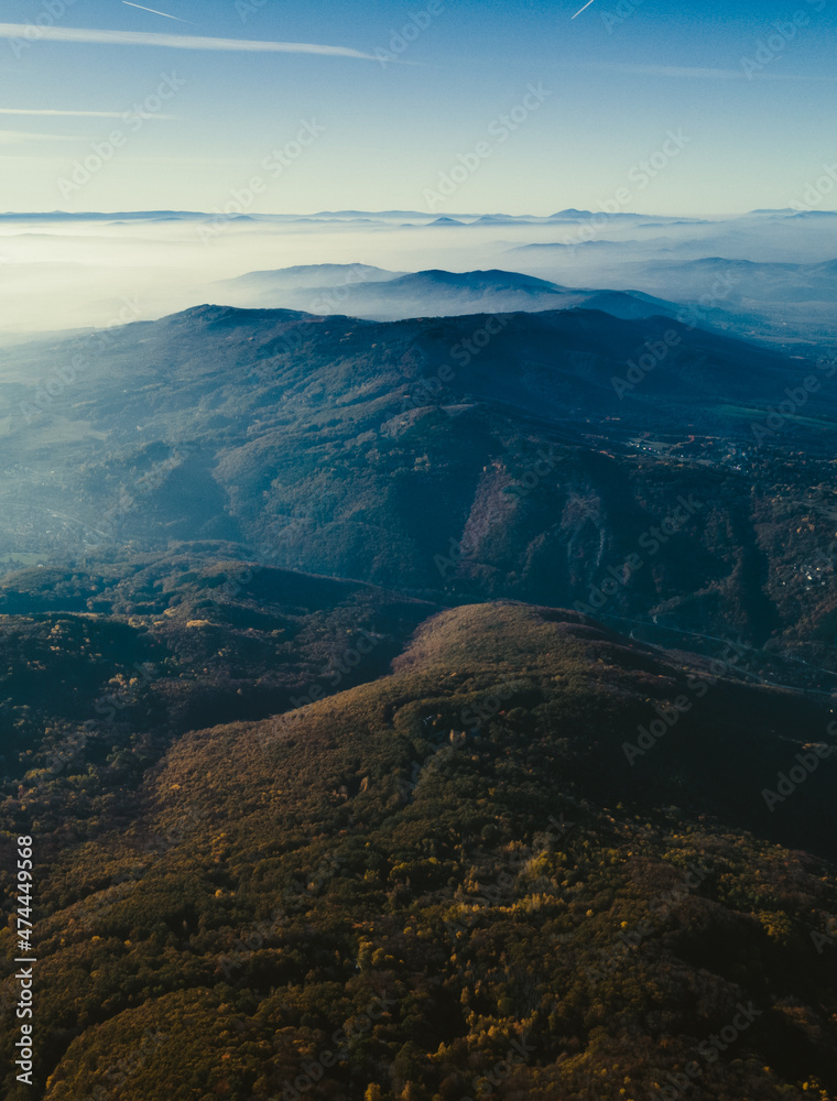 Obraz premium Mountain view with mist over autumn trees. Stunning view with blue sky, bright shining sun and white clouds. High quality photo