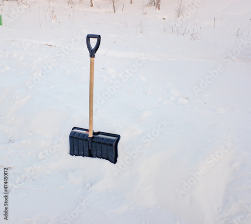 a black plastic shovel with a wooden handle stuck in fluffy white snow