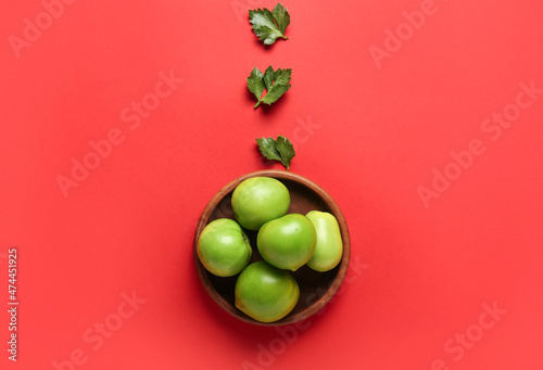 Composition with bowl of green tomatoes and parsley on color background