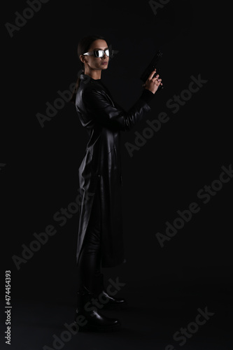 Woman with gun dressed in matrix style on dark background