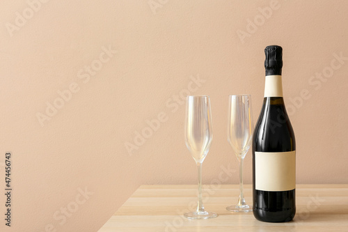 Bottle of champagne and glasses on wooden table near color wall