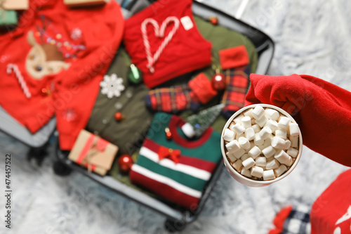 Woman drinking hot chocolate and packing suitcase at home. Christmas holidays concept