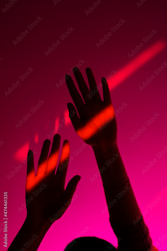 Closeup of anonymous woman arm gesturing with open hand over fashion blue, orange and pink wall background, neon red stripe on wrist. Colorful light, minimalism concept. 