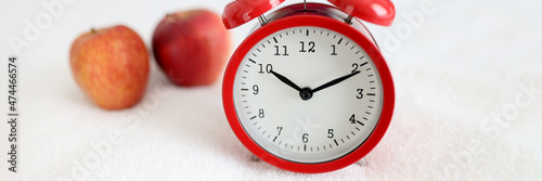 Red alarm clock standing on white towel near apple closeup