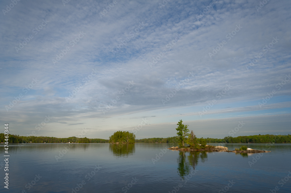 Landscape panorama of a calm lake in the Kawarthas, Ontario Cottage Country. Cottages nestled among green trees are visible across the blue waters.