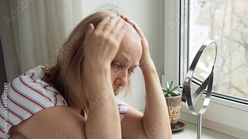 Aging woman upset with gray hair looking in mirror.