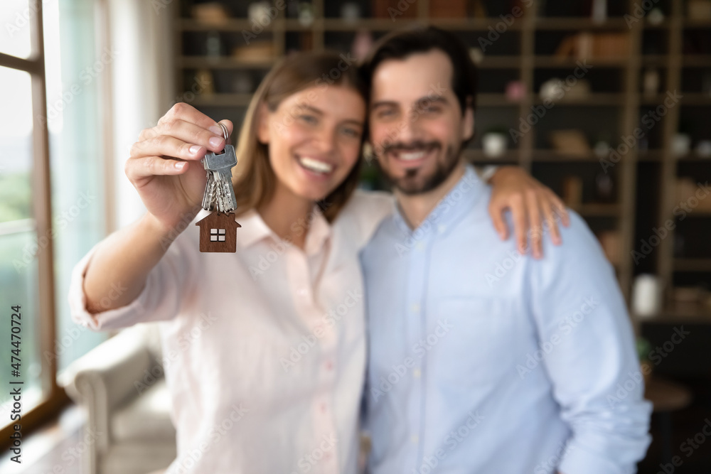 Happy young family couple of tenants receiving, holding keys from new home, hugging, celebrating real estate purchase. Husband and wife, new homeowners excited with apartment buying. Close up of hand