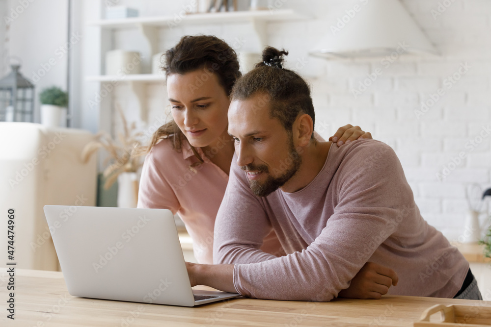 Young millennial married couple using online app on laptop at kitchen table, paying domestic bills, mortgage insurance fees, taxes. Dating girl and guy browsing, shopping on internet at home Young millennial married couple using online app on laptop at kitchen table, paying domestic bills, mortgage insurance fees, taxes. Dating girl and guy browsing, shopping on internet at home