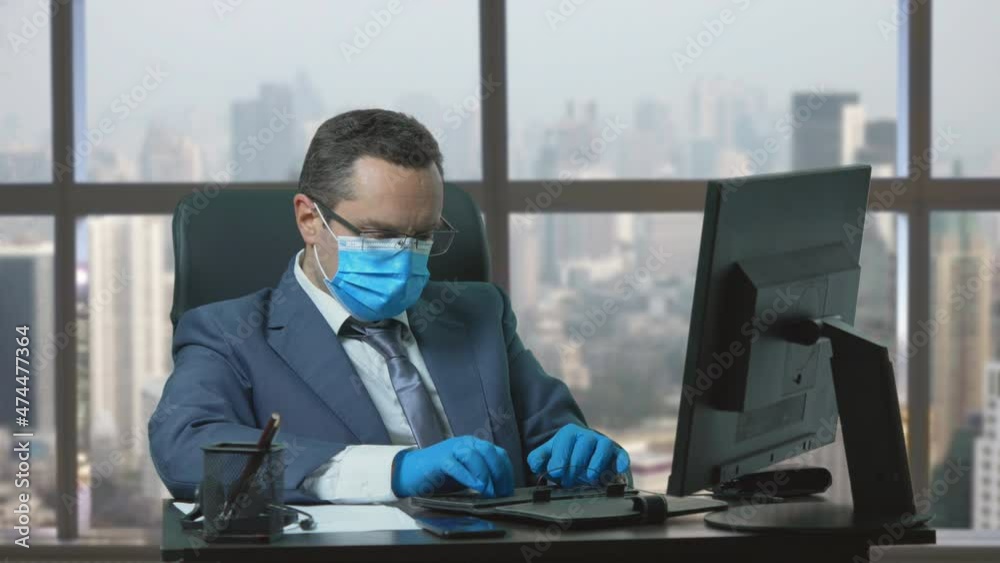 Businessman with gloves and corona virus task at computer , office window view Businessman with gloves and corona virus task at computer , office window view
