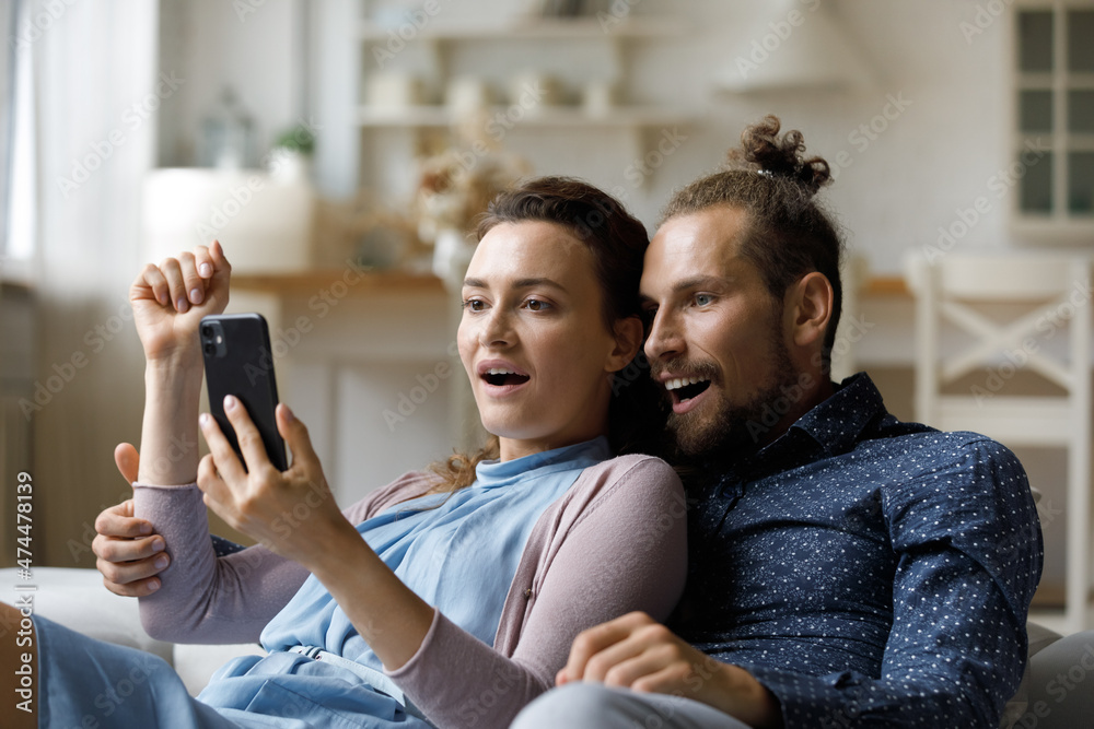 Excited surprised millennial dating couple getting unexpected news on smartphone, reading text message, staring at screen together with shocked amazed faces. Happy girl and guy using mobile phone Excited surprised millennial dating couple getting unexpected news on smartphone, reading text message, staring at screen together with shocked amazed faces. Happy girl and guy using mobile phone