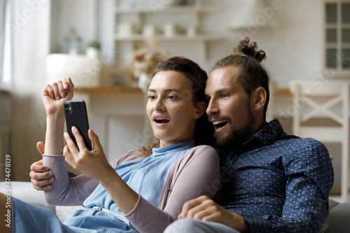 Excited surprised millennial dating couple getting unexpected news on smartphone, reading text message, staring at screen together with shocked amazed faces. Happy girl and guy using mobile phone