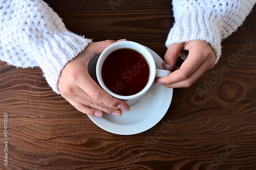 girl's hands in warm knitted white sweater are holding cup of tea. Flat lay with top view on wooden background