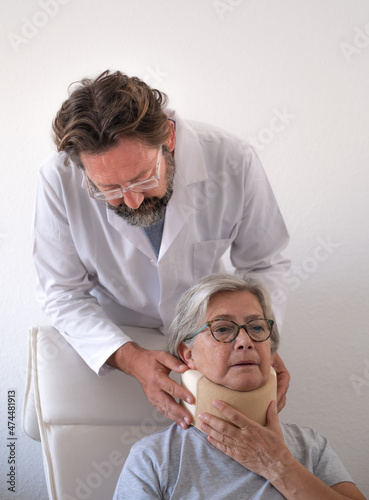 Senior woman in pain wearing a cervical collar with the assistance of her physiotherapist doctor