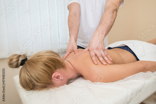 Male masseur massaging back and shoulder blades of young woman lying on massage table on white background.