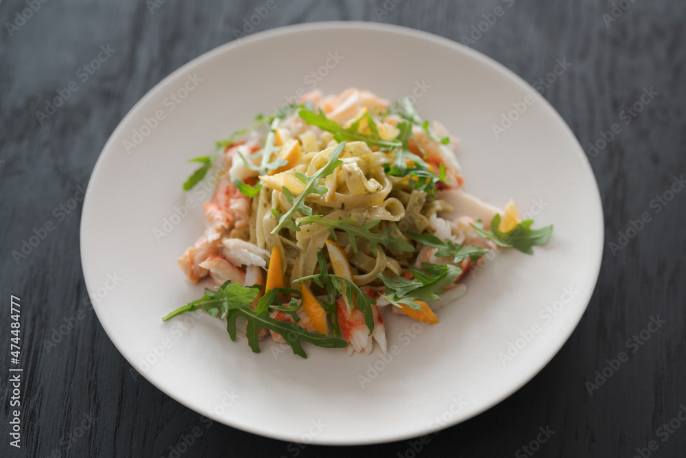 Fettuccine pasta with crab and arugula on black wood table Fettuccine pasta with crab and arugula on black wood table