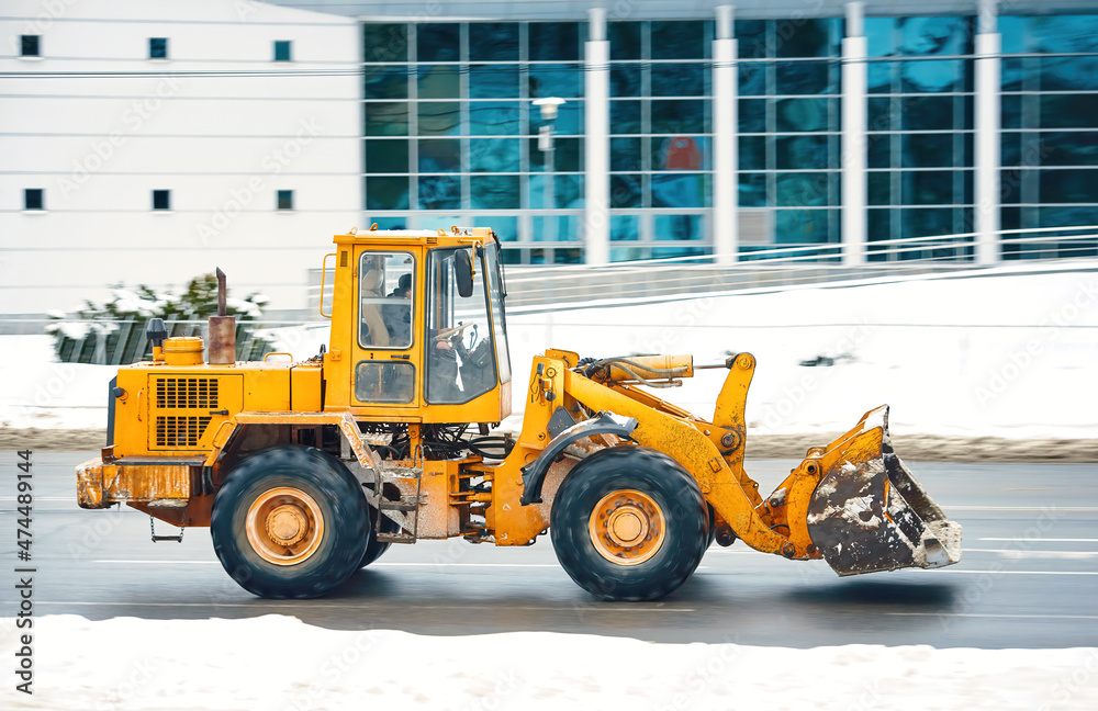 Wheel loader riding on road, snow removing vehicle. Snow cleaning machine . Heavy duty wheel loader moving on city road, clear snow after heavy snowfall. Wheel loader riding on road, snow removing vehicle. Snow cleaning machine . Heavy duty wheel loader moving on city road, clear snow after heavy snowfall.