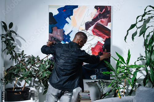 African american painter hanging his abstract colorful piece on the wall.